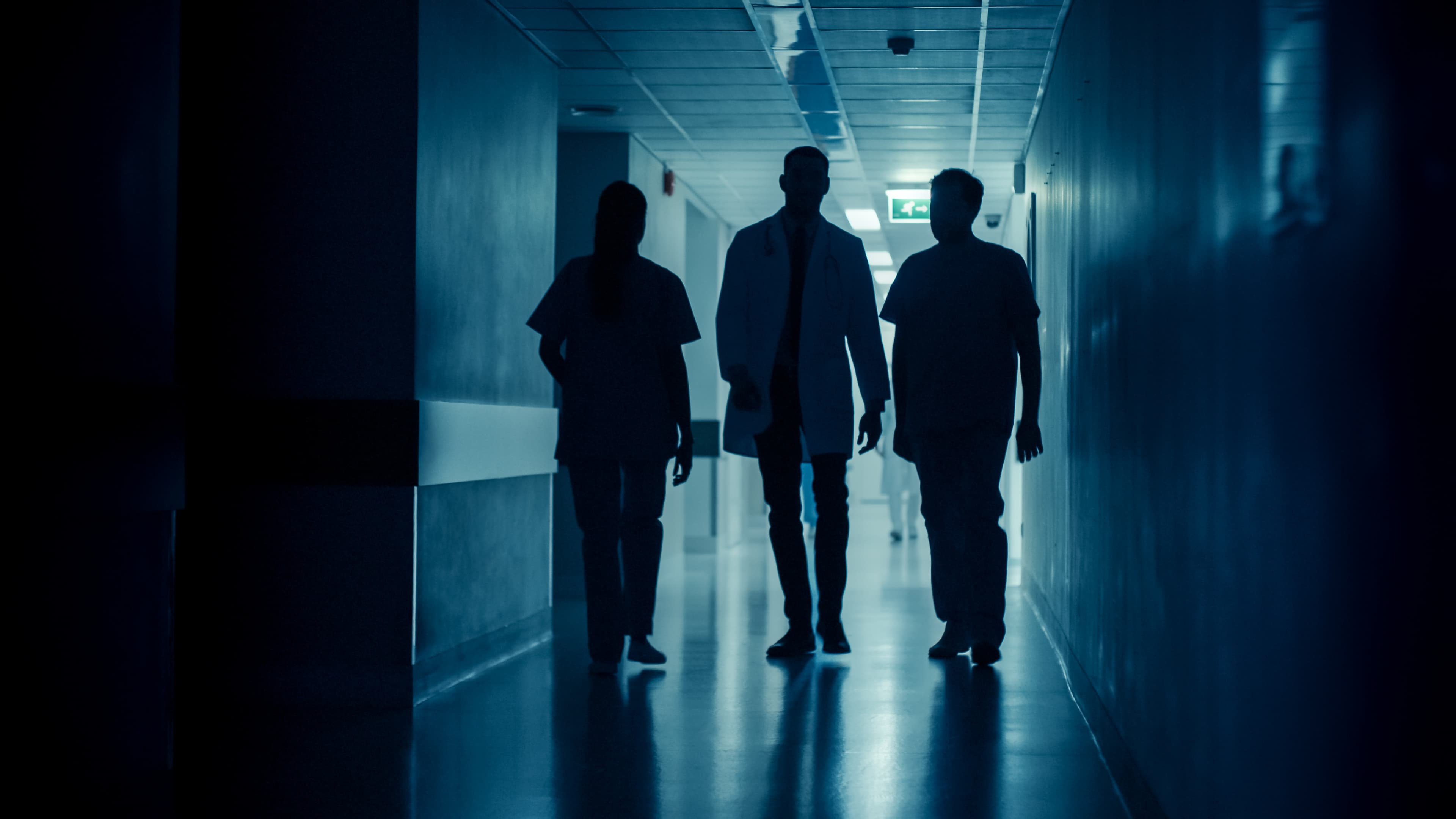 Silhouettes of Surgeon and Doctor Walk Through Dark Hospital Hallway. Modern Hospital with Professional Staff.