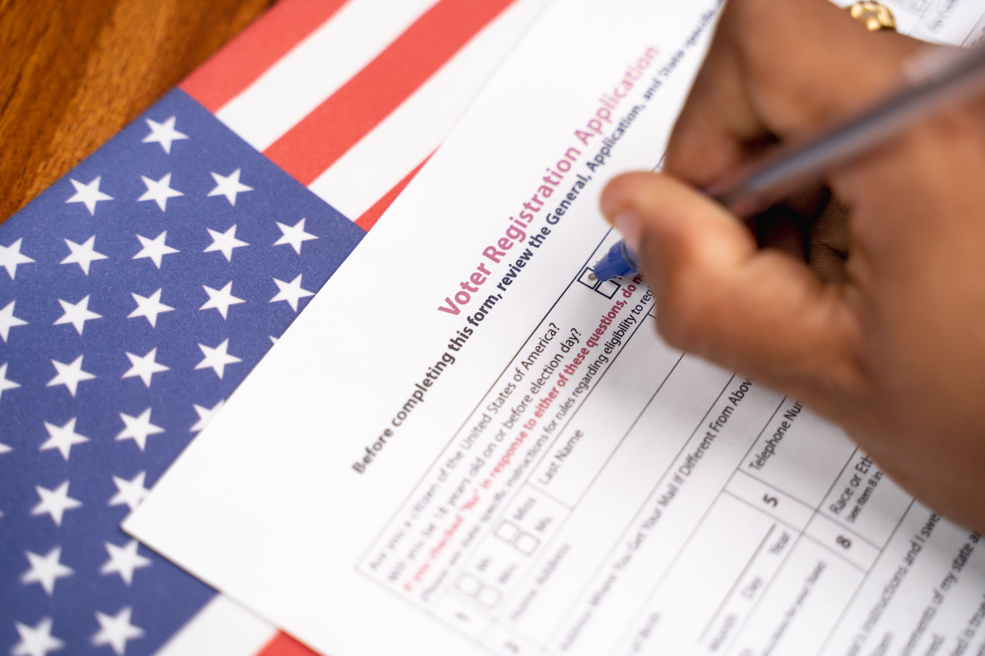 Close up of hands filling President voter Registration Application with US flag as background for upcoming election.