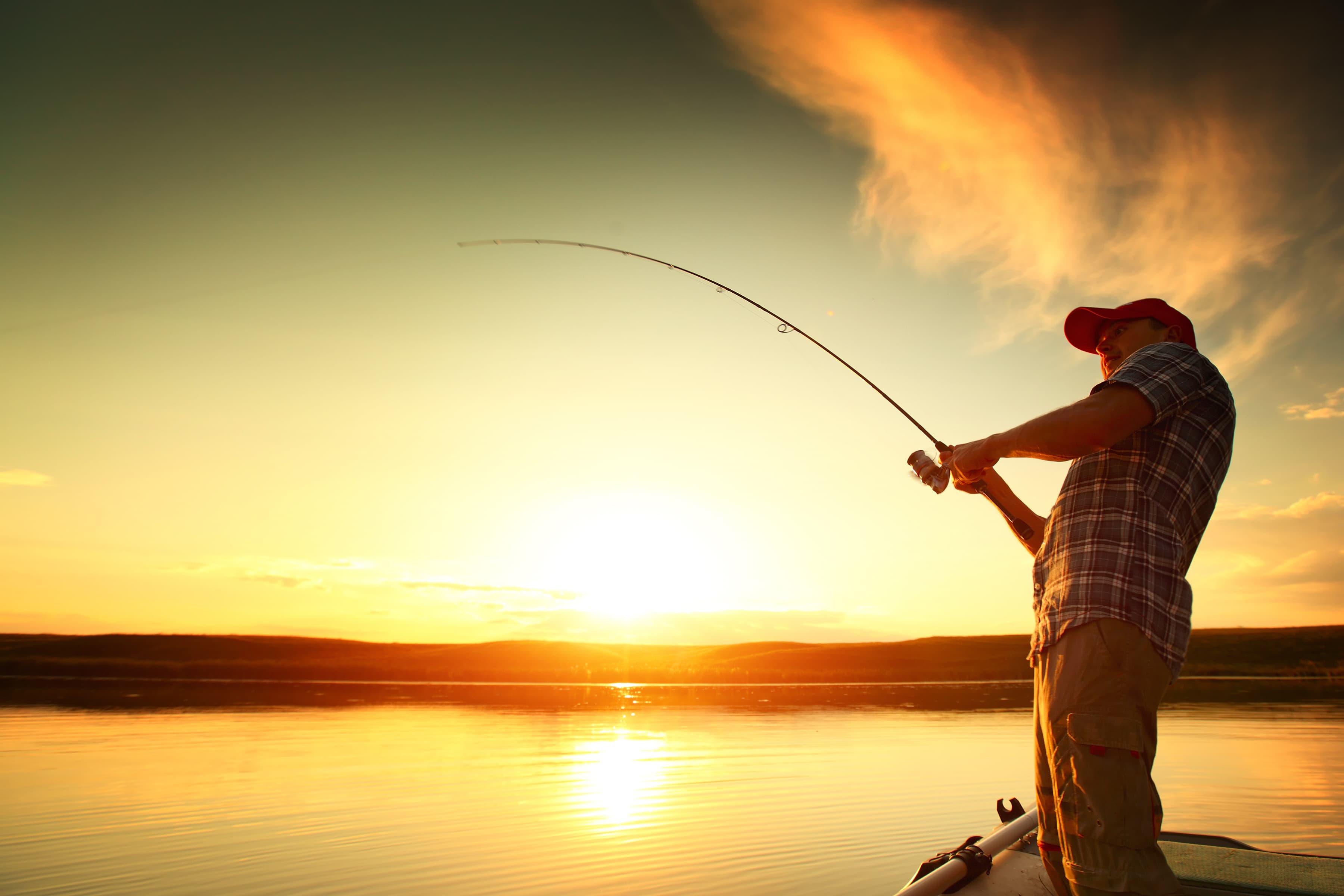 Young man fishing on a lake from the boat at sunset