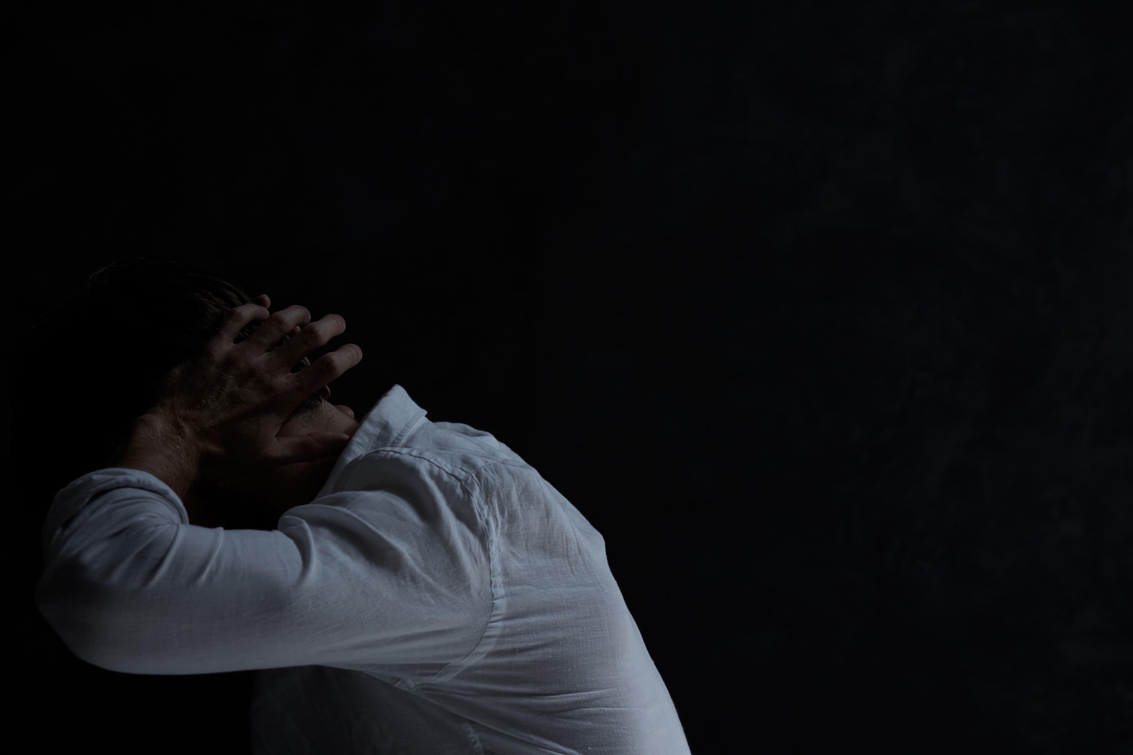 Despair man covering his ears, sitting in dark room