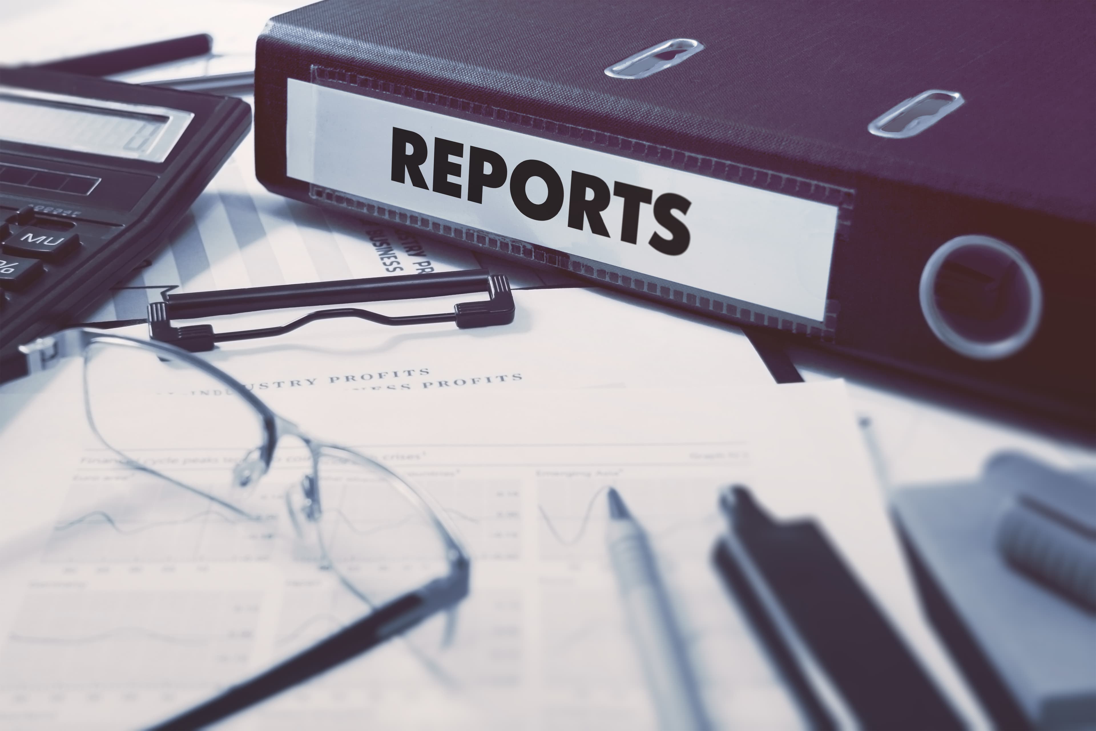 Ring Binder with inscription Reports on Background of Working Table with Office Supplies, Glasses, Reports. Toned Illustration. Business Concept on Blurred Background.