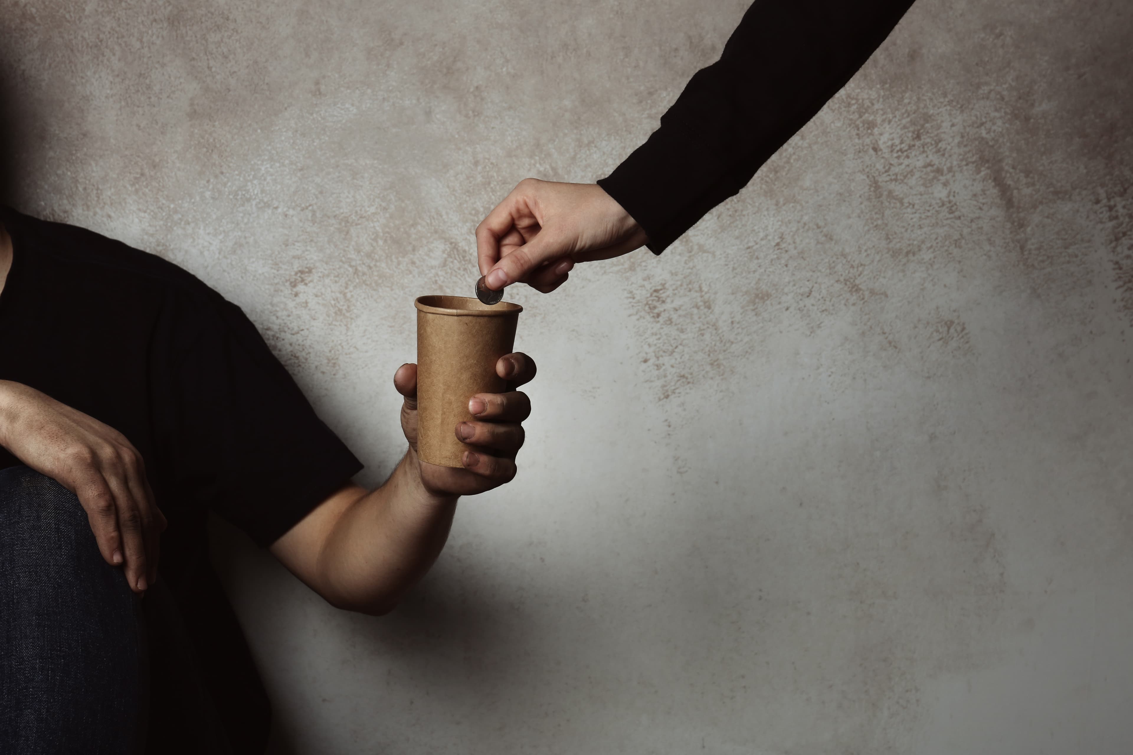 Poor man receiving coin from woman on grey background with space for text, closeup