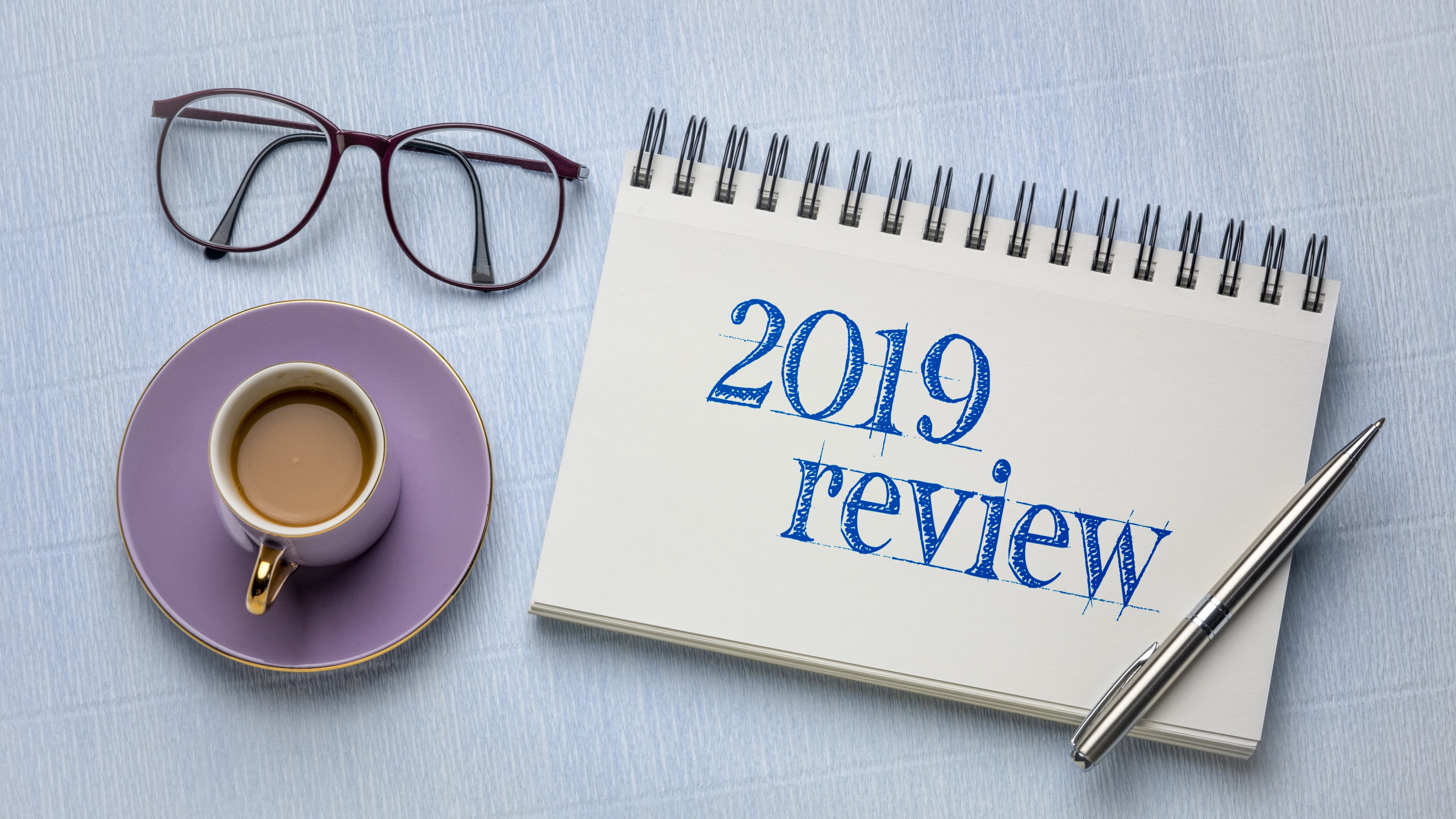 2019 review text in a spiral notebook with a pen, coffee and reading glasses, business year summary and evaluation concept