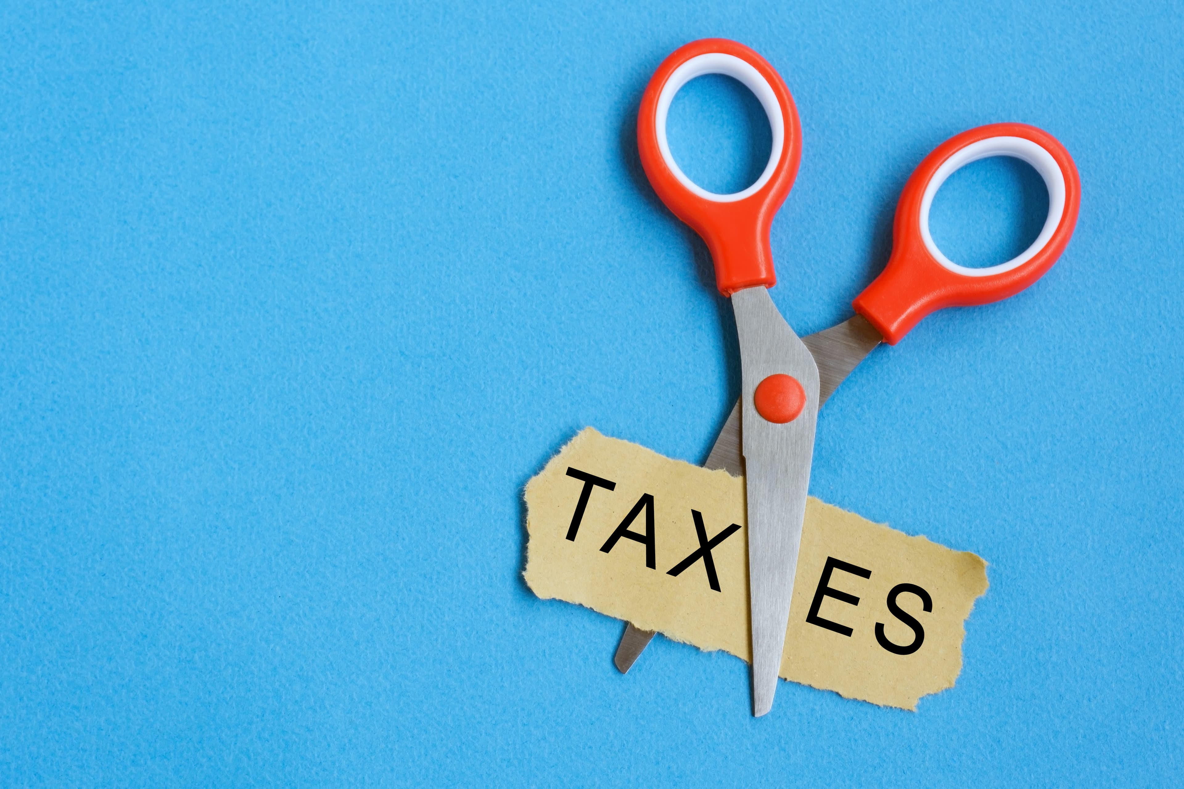 Scissor cutting the word 'taxes' in a piece of paper.