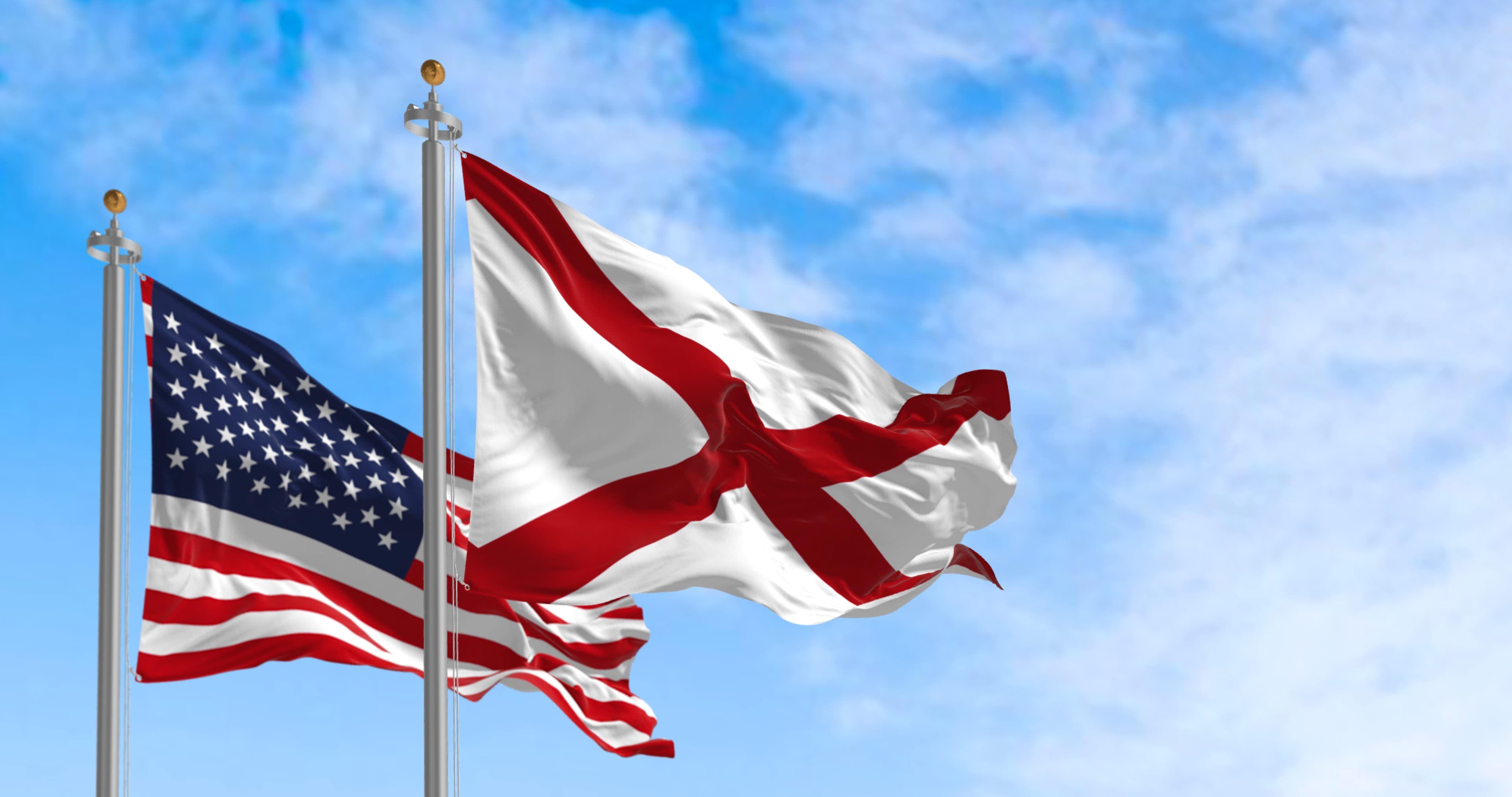 The flag of the state of Alabama waving alongside the national flag of the United States on a sunny day