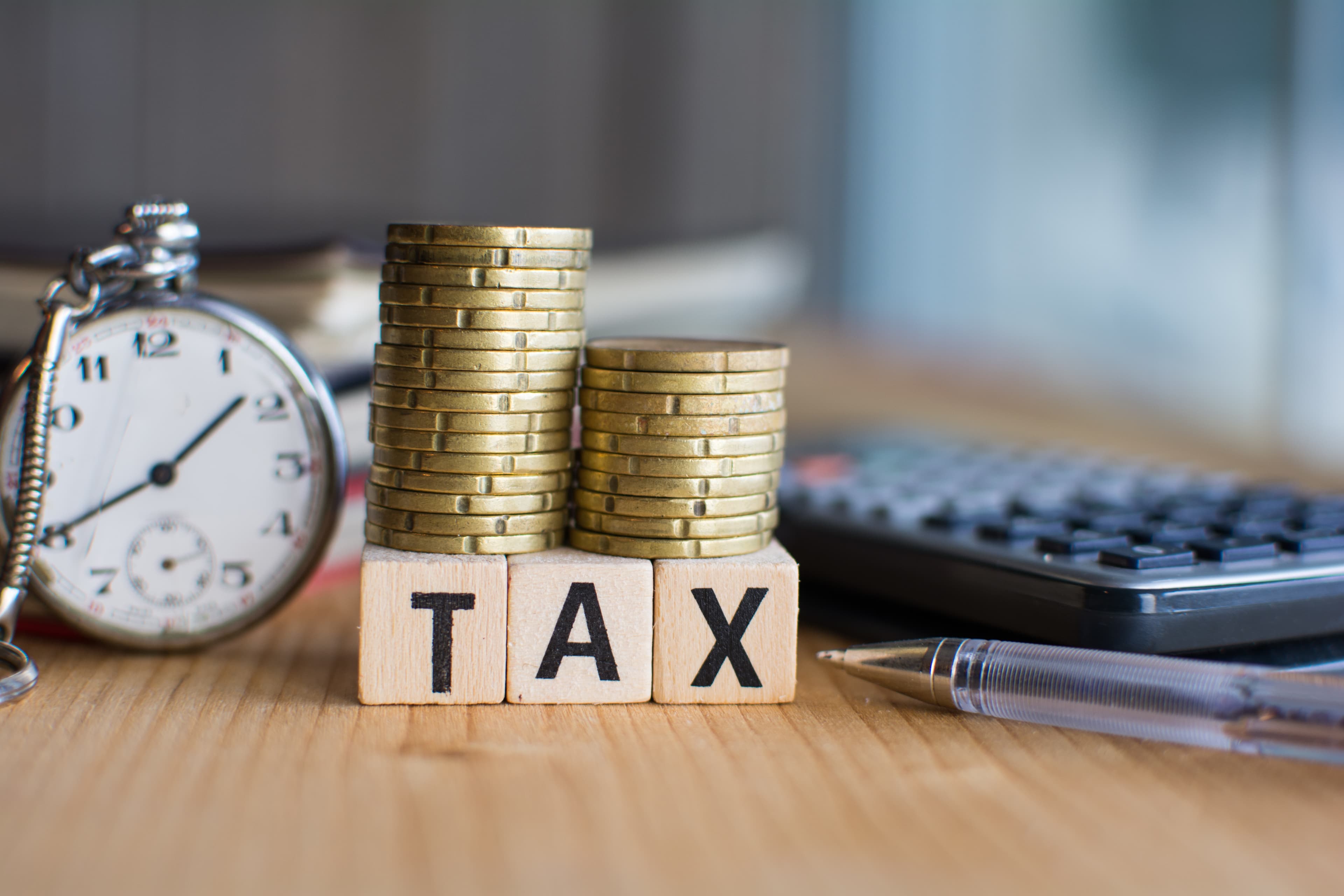 Close-up Of the word Tax On Wooden Blocks and a pocket watch and a calculator on the background