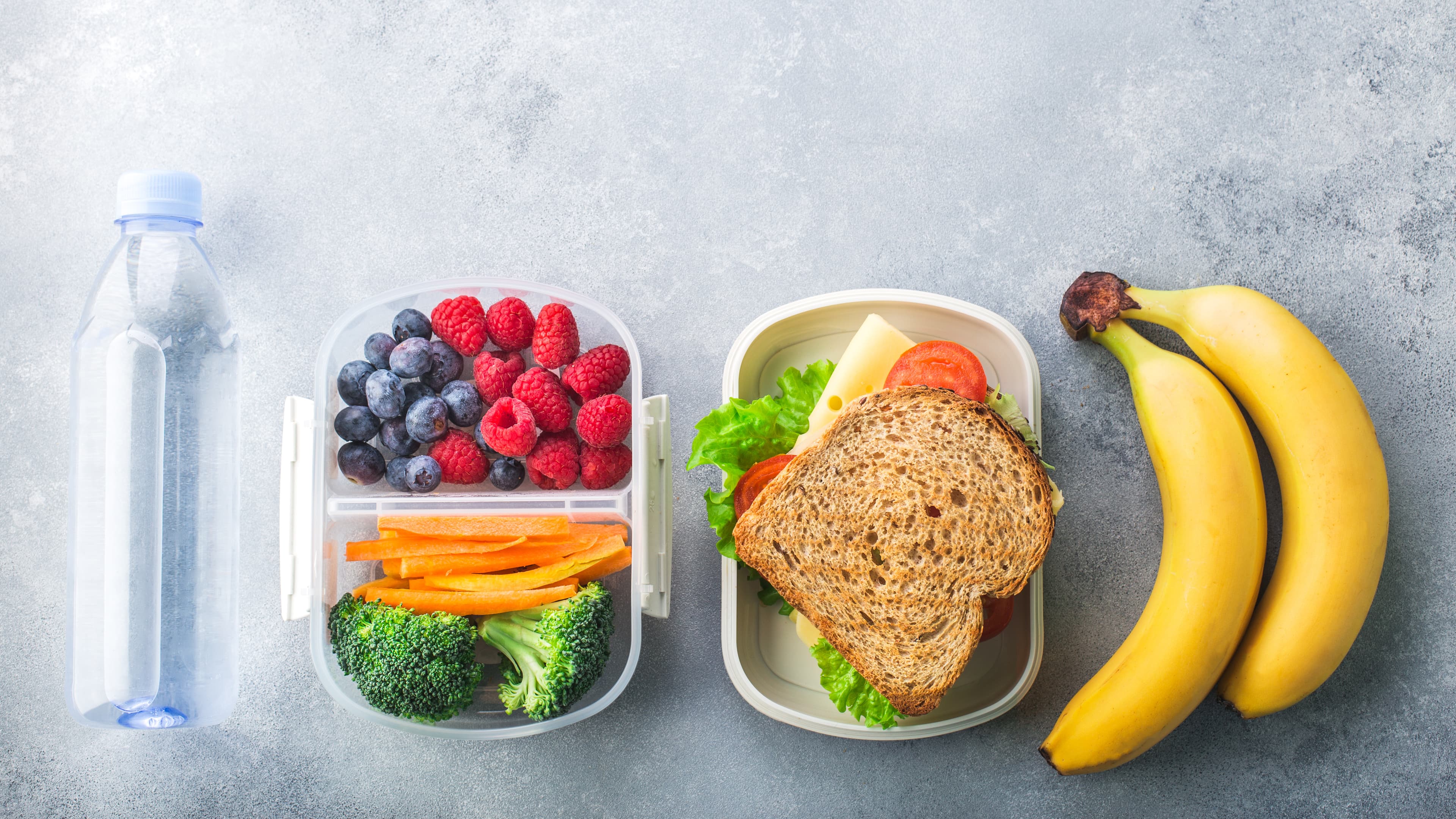 School lunch box with sandwich vegetables water almonds and fruits on black chalkboard