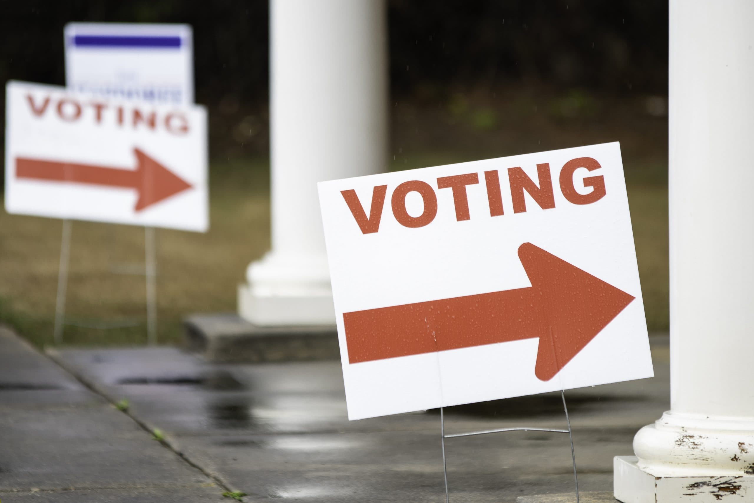 Close up of voting signs pointing toward the polling location on a rainy day.