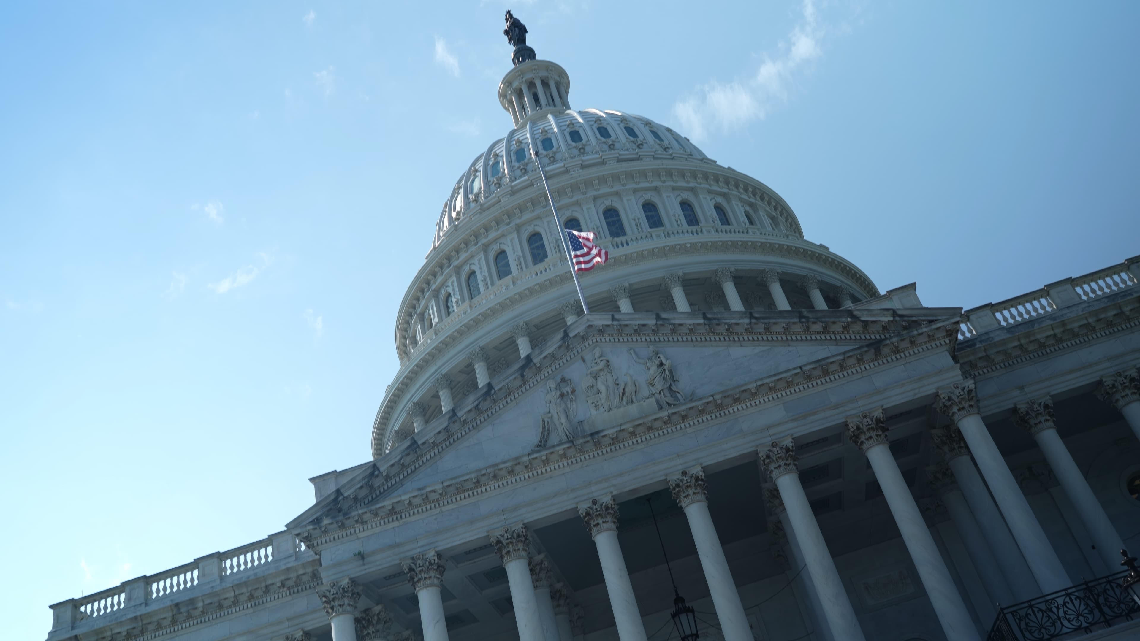 Angle view of the US Capitol dome with flag at half mast feeling chaos, tilted angle, seat of government in Washington, DC on a beautiful sunny day with clear blue sky.
