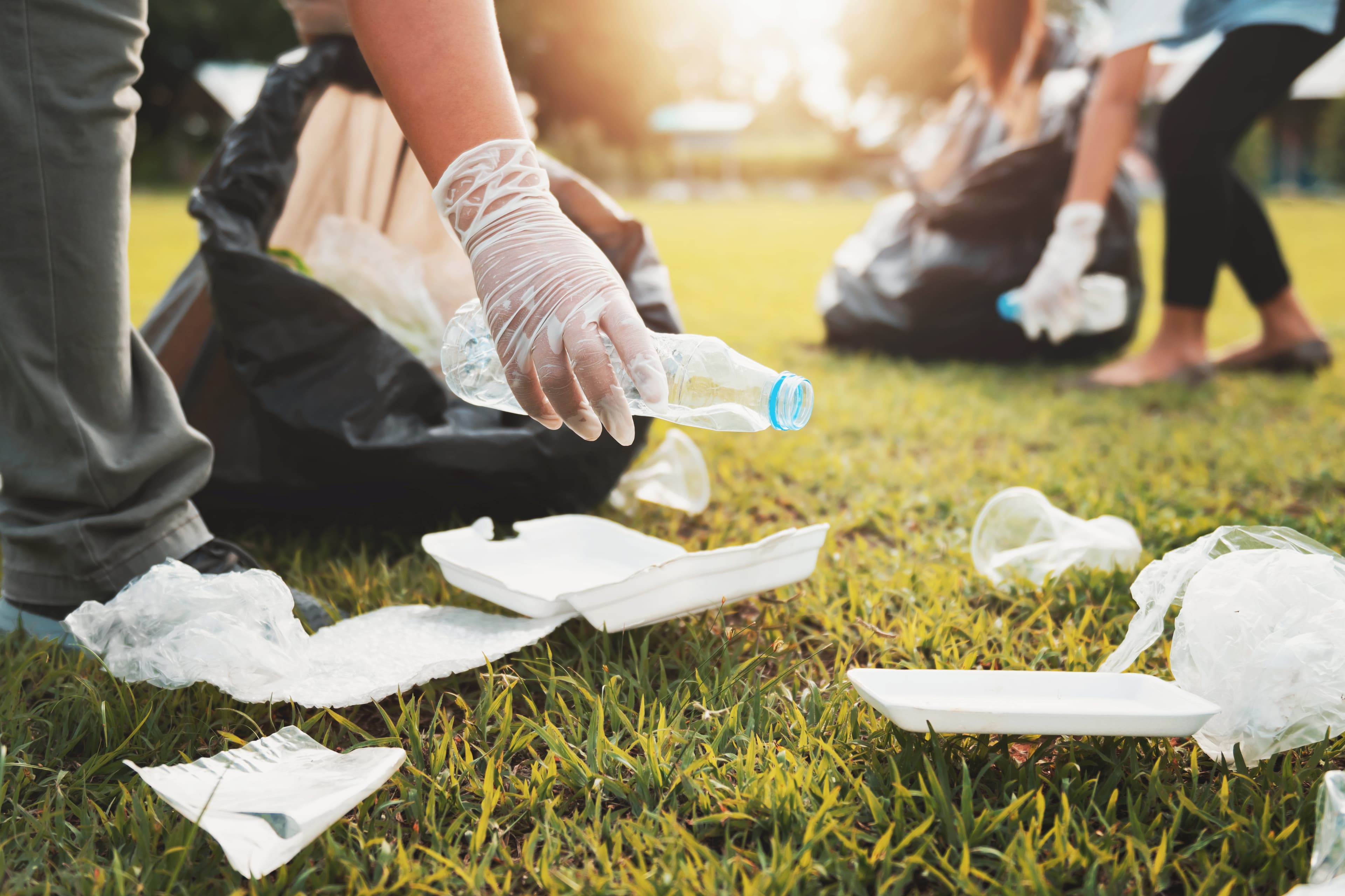mother and children keeping garbage plastic bottle into black bag at park in morning light