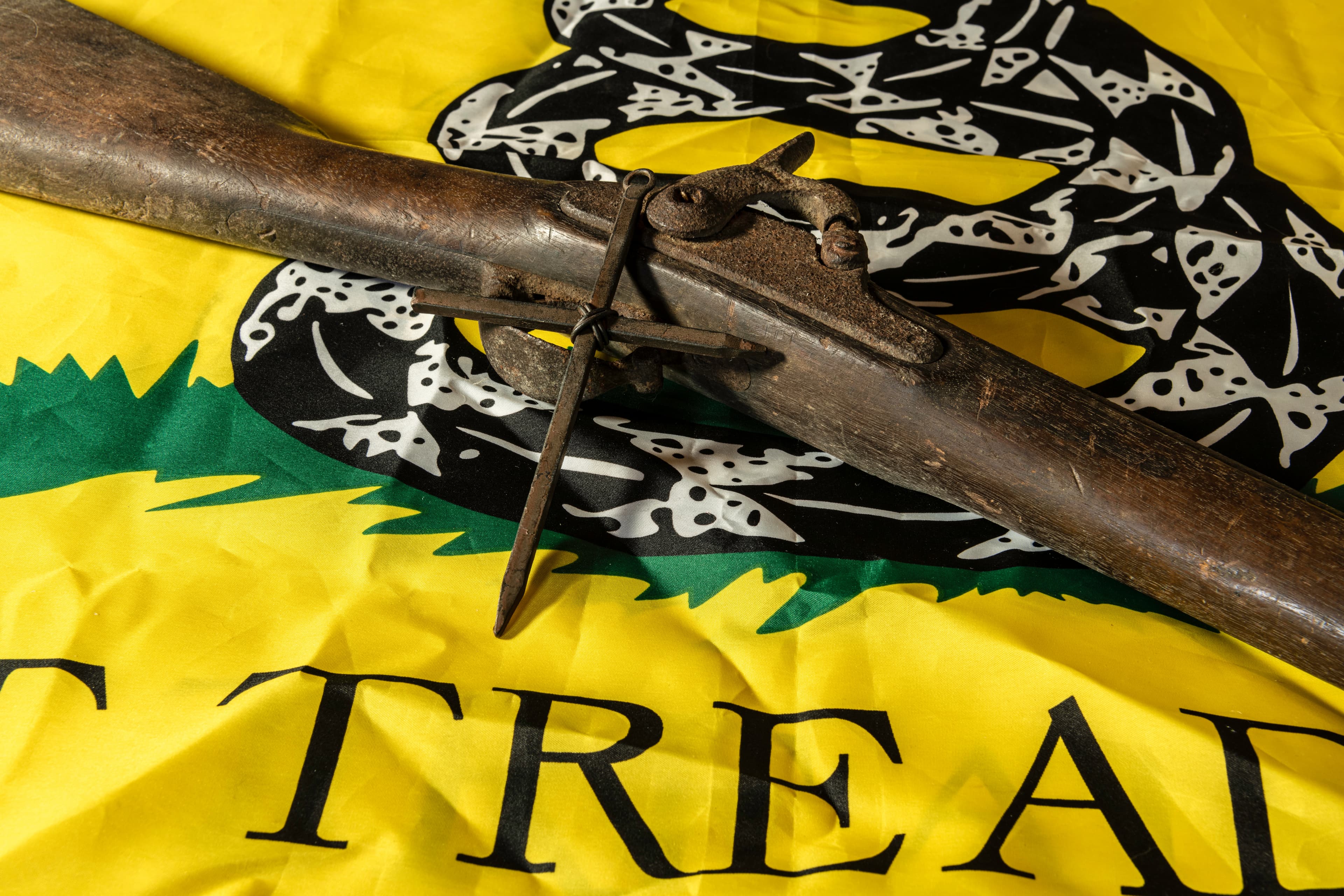 old musket gun with metal cross on yellow don't tread om me Gadsden flag