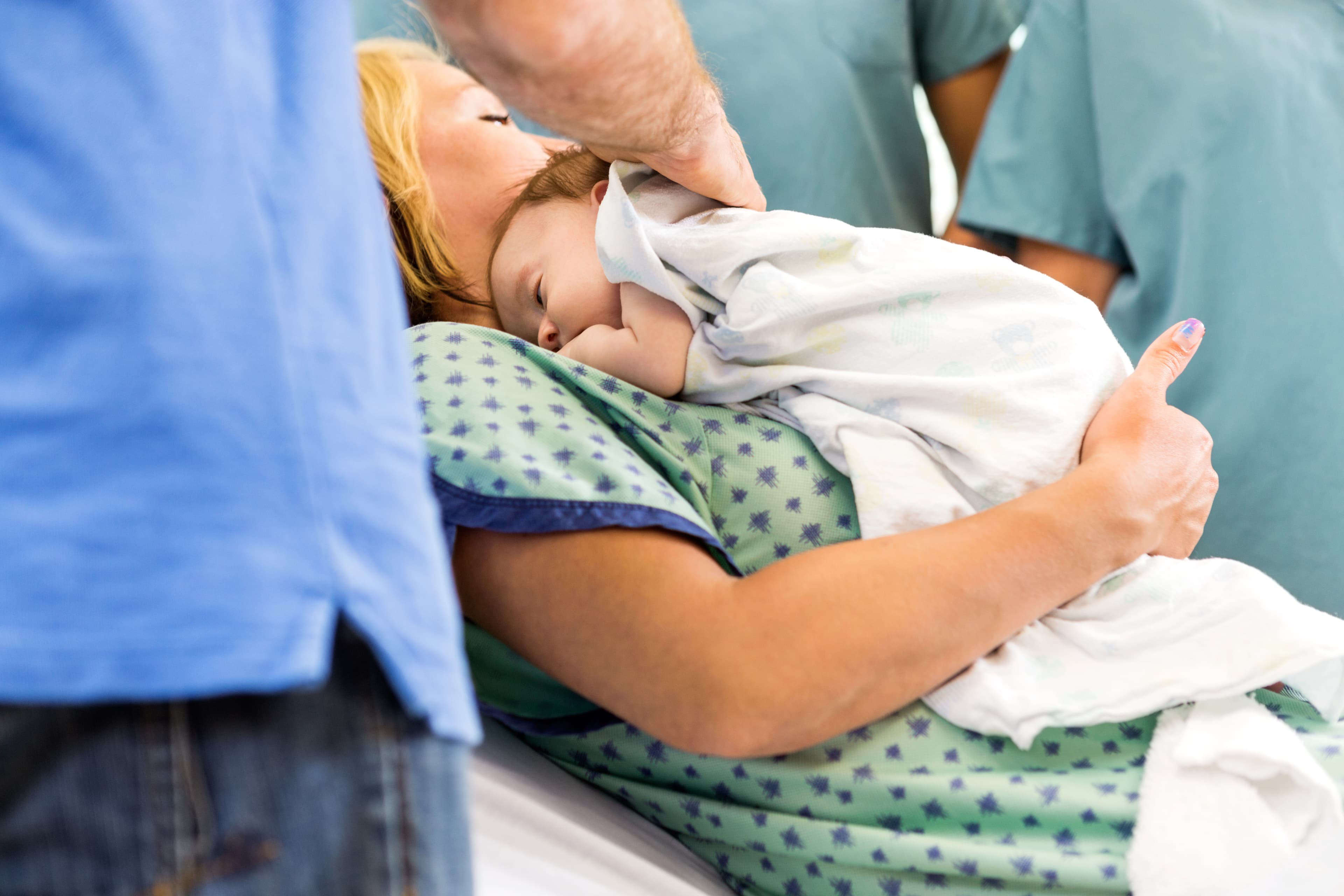 Newborn babygirl lying on mother surrounded by nurses and father in hospital