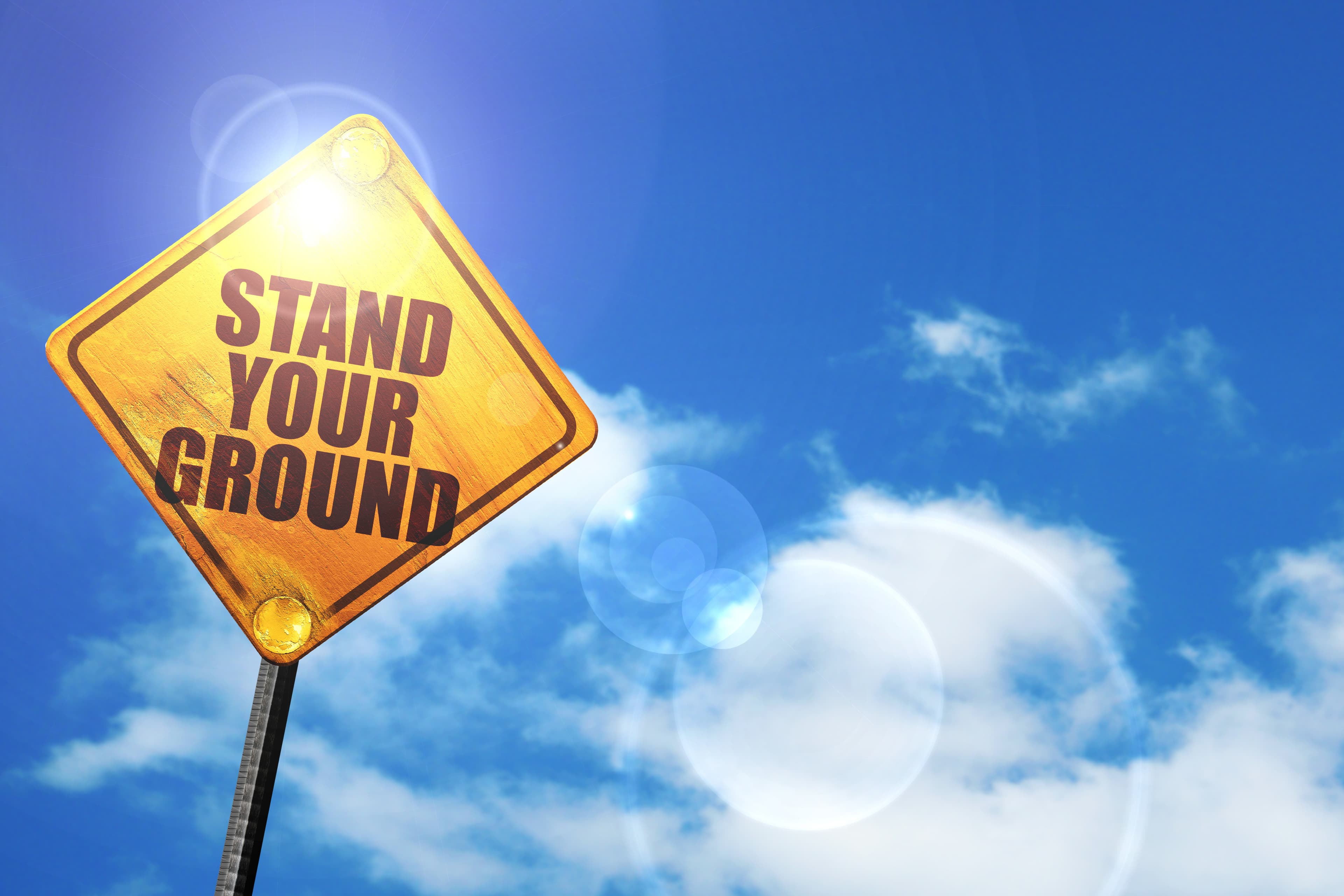 stand your ground: yellow road sign with a blue sky and white clouds