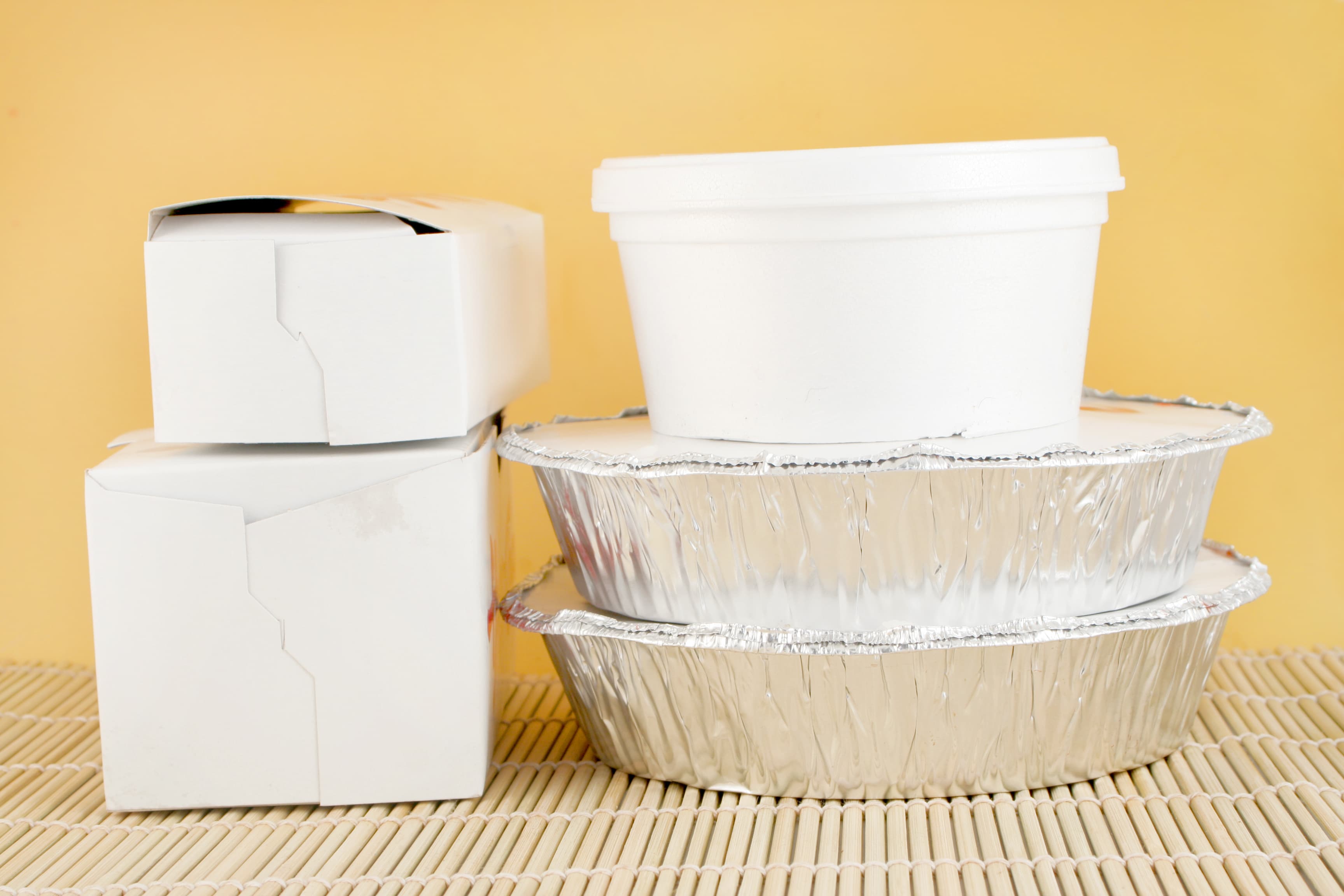 chinese food delivery or takeout aluminum covered containers and cardboard boxes on bamboo placemat