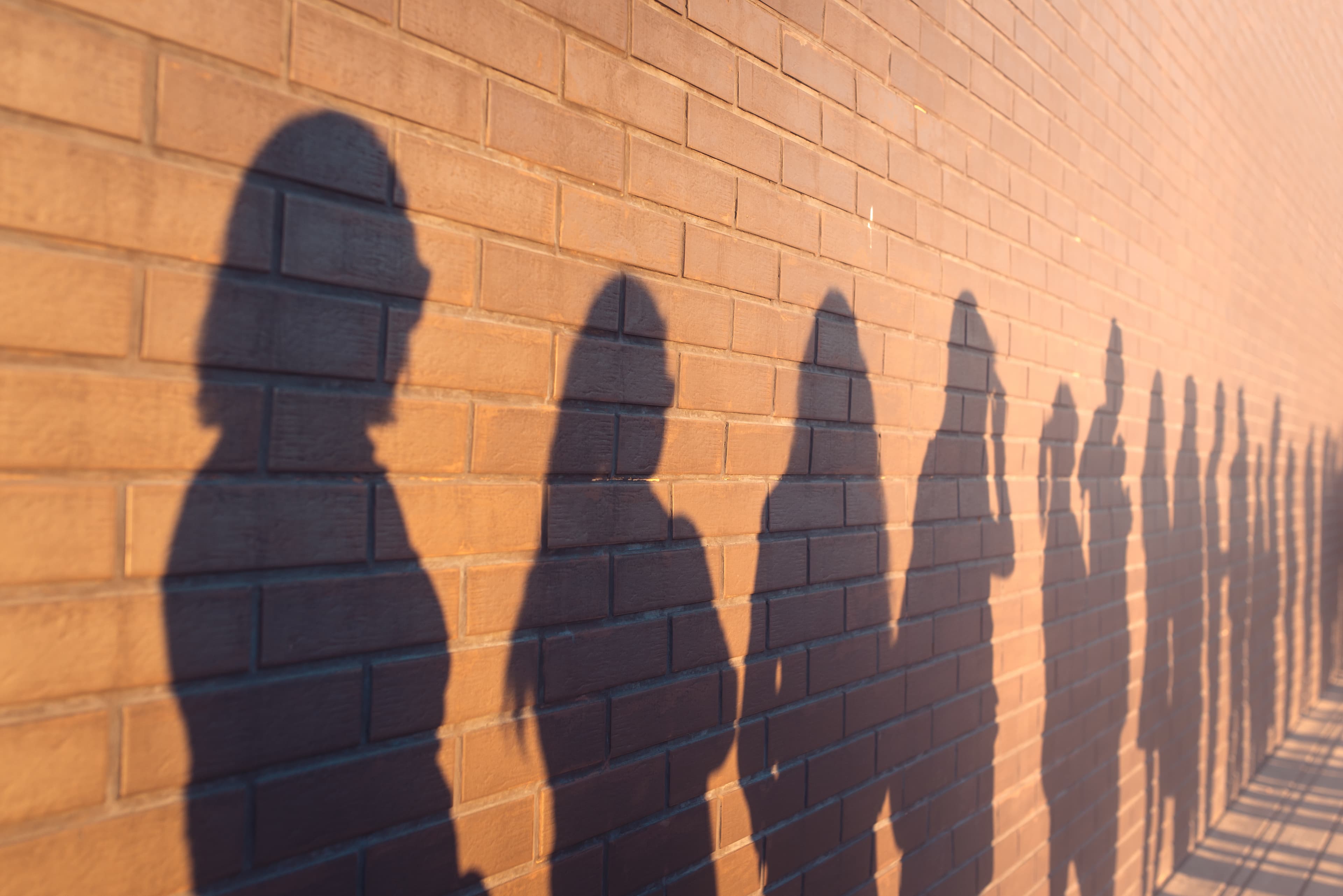 a line of shadows of people lined up against a red brick wall. Stand in a queue to the changes.